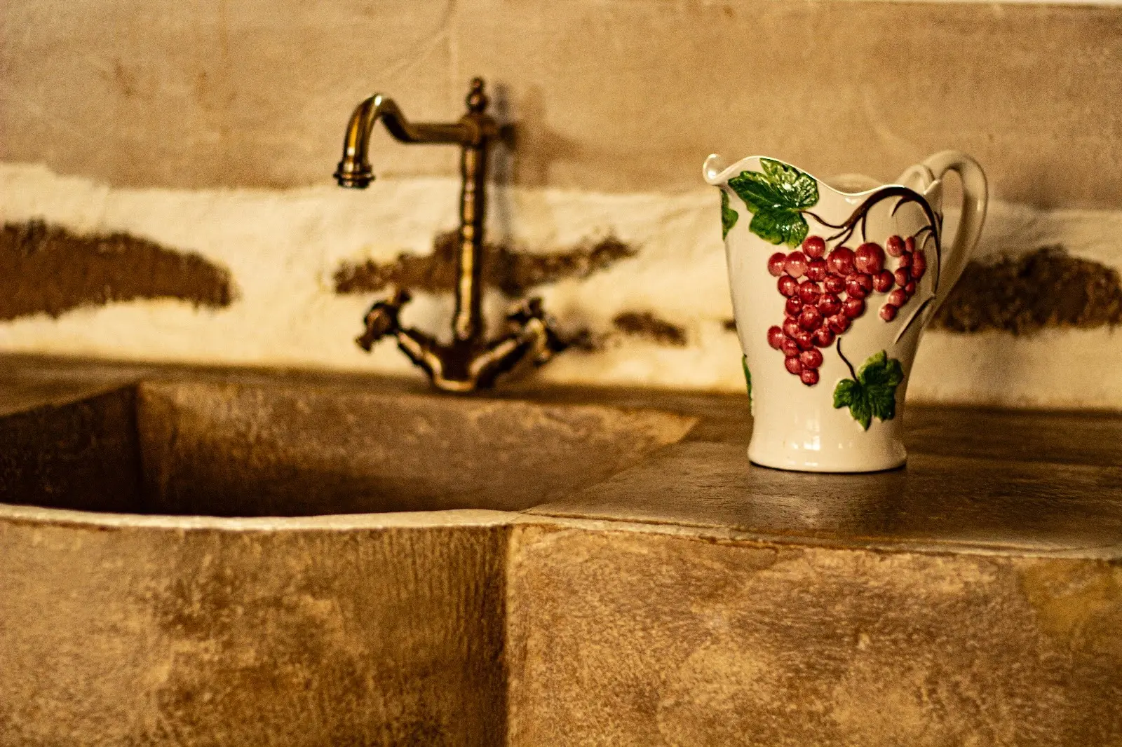 L’évier taillé dans la pierre, son robinet en laiton et un pichet ancien décoré de grappes de raisin.