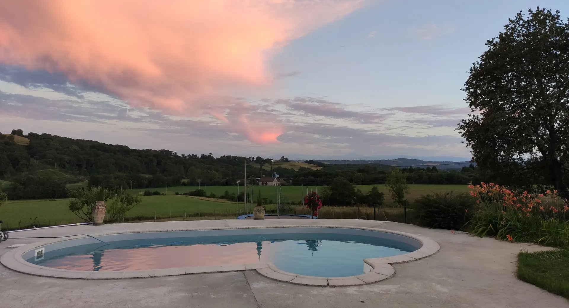 La piscine du gîte au coucher du soleil, nuages roses, collines béarnaises à l’horizon.